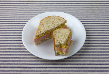 Pressed pork canned meat sandwich on wheat bread on a white plate atop a blue striped tablecloth.