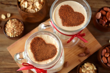 Milkshake decorated with cinnamon heart in glass vessels. Top view. Peanuts are around