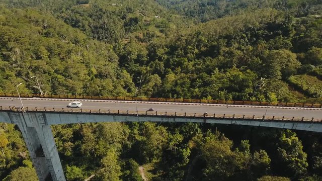 Bridge with car road over mountain canyon, mountains, rainforest. Aerial view of bridge in a mountain gorge above a green jungle among the mountains. Bali, Indonesia. 4K video. Aerial footage.
