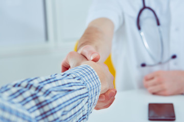Close up of a male doctor shaking hands with his male patient. Medicine and trust concept