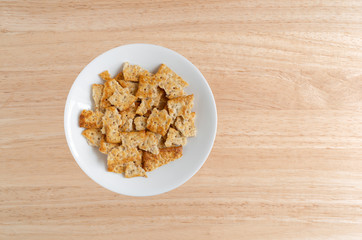 Broken flatbread salted multigrain crackers on a white plate atop a wood table.