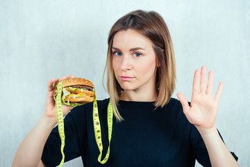 young and attractive blond woman in black T-shirt and measuring tape is holding a high-calorie...