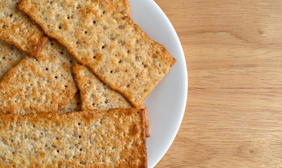 Top close view of flatbread salted multigrain crackers on a white plate atop a wood table top.