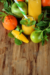 Yellow smoothie in glass jars surrounded by fruits and mint against wooden background
