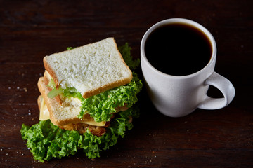 Breakfast table with sandwich and black coffee on rustic wooden background, close-up, selective...