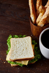 Breakfast table with sandwich and black coffee on rustic wooden background, close-up, selective focus