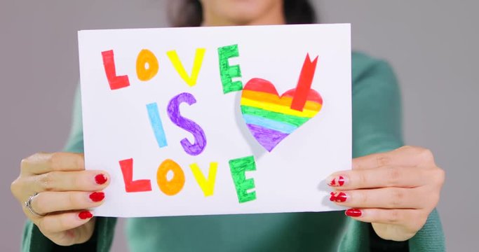 LGBT day concept. Unknown woman showing a paper with a LGBT flag rainbow heart shape in the studio, shot in 4k resolution
