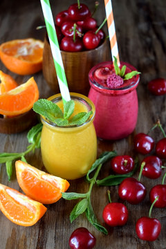 Yellow and red smoothies in glass jars surrounded by mandarins and cherries