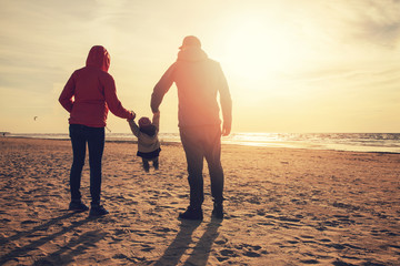 mother and father swinging child by the arms on the beach at sunset