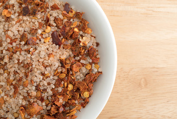 Top close view of Greek spice rub in a white bowl atop a wood table.