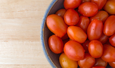 Top close view of a bowl filled with grape tomatoes on a wood table.