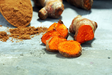 Turmeric powder and fresh turmeric on grey background