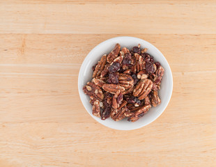 Sugar glazed pecans with dried cranberries in a white bowl atop a wood table top.