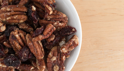 Top close view of sugar glazed pecans with dried cranberries in a white bowl atop a wood table.