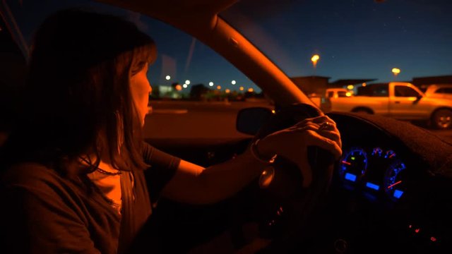 A middle aged woman backing up her car at night