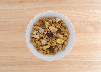 Top view of fruit mix granola in a bowl atop a wood table.