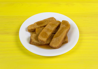 French toast sticks on a white plate with syrup atop a bright yellow table top.