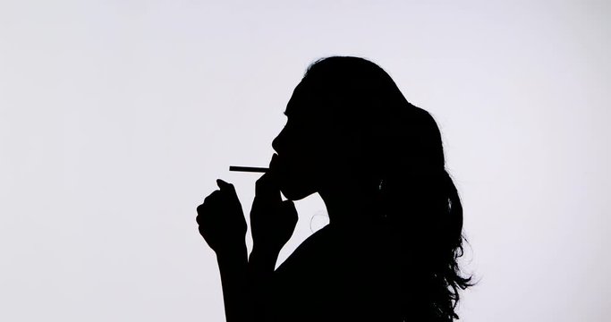Silhouette of young woman enjoying a cigarette in the studio, isolated on white background. Shot in 4k resolution