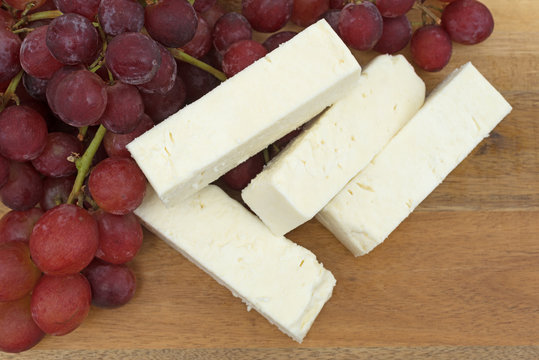 Close view of Feta cheese slices with fresh red grapes on a wood cheese board.