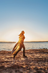 young blond girl with fluttering hair and clothes running along the beach in bright highlights...