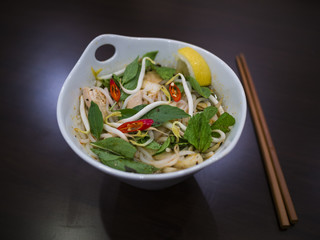 Beautiful and appetizing photo of a traditional vietnamese chicken noodle soup, also know as Pho Ga. In a white bowl with wooden background and luxurious wooden chopsticks.