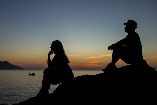 Silhouette of quarreled couple at sunrise seating on the rocks.