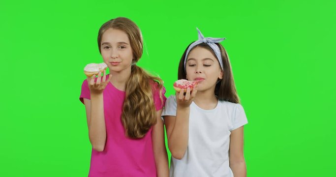 Cute teenagers in the pink and white T-shirts holding donuts, biting them and eating. Green screen. Chroma key.