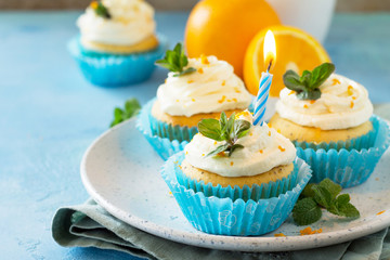 Orange Birthday cupcake with buttercream icing and candle on a blue a stone or slate background. Copy space.