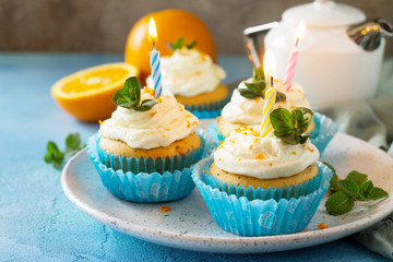 Colorful orange cupcake with birthday candle on a blue a stone or slate background.