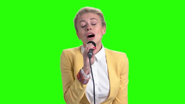 Young pretty blonde singing with microphone. Elegant girl holding microphone and singing on chroma key background. Beautiful caucasian singer.