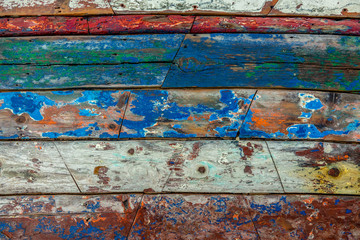 Fototapeta na wymiar Surface of old and worn out wooden panels painted in several colours with the apaint peeling off