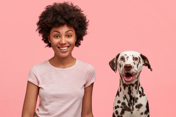 Positive African American female with glad expression and her dalmatian dog being satisfied after...