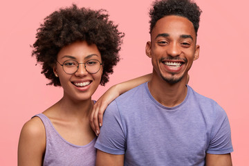 Glad dark skinned female with positive expression, spends free time with her groupmate, smile positively after successfully passed session, isolated over pink background. Lovely African couple