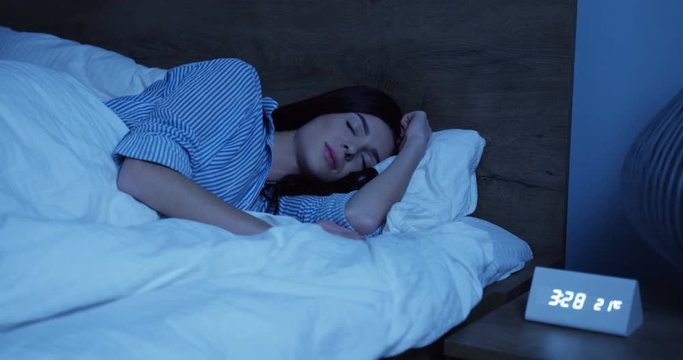 Portrait shot of the young Caucasian woman in the blue pajama dreaming while sleeping in the bed at night and moving from side to side. Indoor
