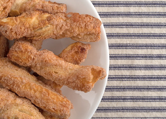 Top close view of crunchy baked twisted cookies on a plate atop a blue striped tablecloth.