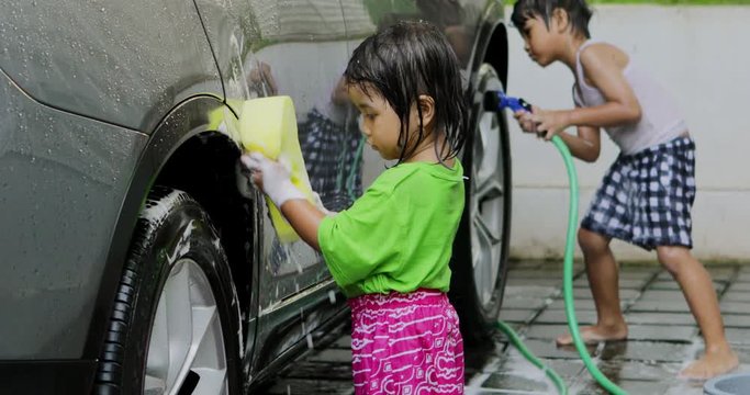 Cute little girl using a sponge to wash a car with her bother at home. Shot in 4k resolution