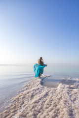 Fototapeta na wymiar Blonde young woman in a blue dress on the shore of the dead sea. Jordan