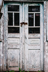 Old wooden door closed on the lock. Peeling paint. Closed on hinges. House. The old door. Paint blue and white.