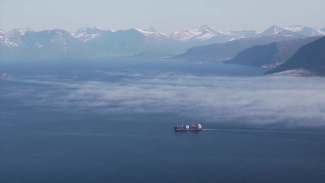 Cargo ship sails in fjords with mist and fog.