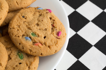 Top close view of candy cookies on a white plate atop a black and white checkerboard tablecloth.