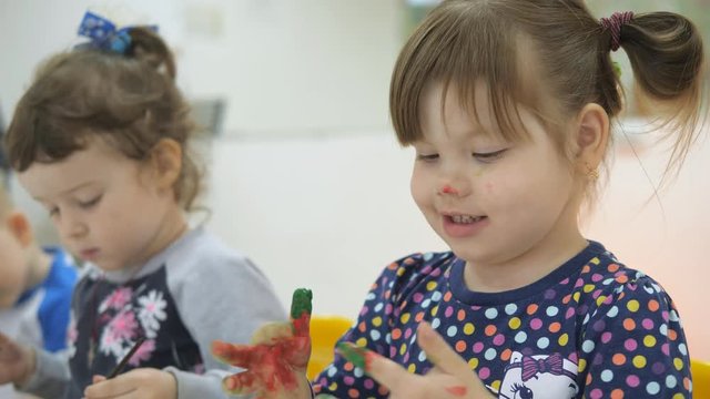 Children's developing a game room. Emotions of young children during entertaining classes. children paint with finger paints on white sheets of paper. girl with a dirty red nose and face, straightens