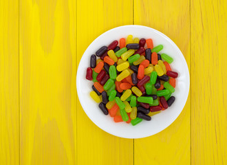 Chewy colorful candy on a white plate atop a bright yellow table.