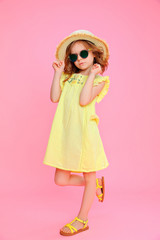 Trendy curly girl in dress and sunglasses wearing straw hat posing on pink.