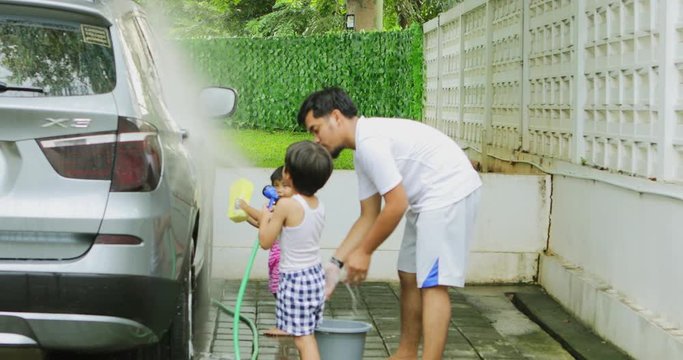 JAKARTA, Indonesia - May 11, 2018: Happy father and his children washing their car together with a water hose outside at home. Shot in 4k resolution