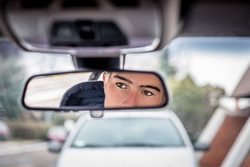 Young handsome man's reflection in the rearview mirror of car. Concept: beauty, fashion,...