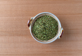 Top view of cilantro flakes in a small bowl on a wood table.