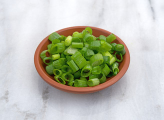 Chopped green onions in a small red clay bowl on a marble cutting board.
