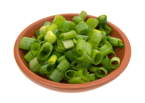 Chopped green onions in a small red clay bowl isolated on a white background.