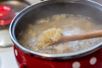 Heart shaped pasta cooked in red pot with white dots on stove. Meal prepared with love. 