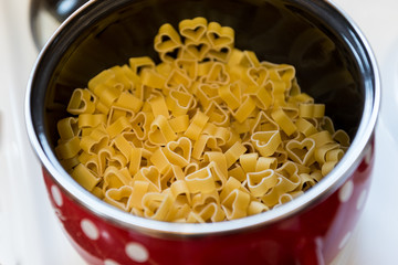 Heart shaped pasta in red pot with white dots on stove. Concept: preparing meal with love
